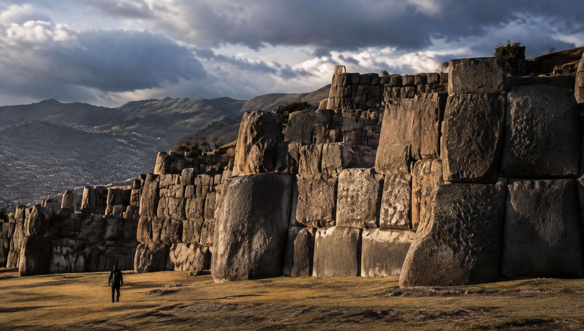 The monumental fitted stone walls of Sacsayhuamán above Cusco in low evening light, a lone figure for scale