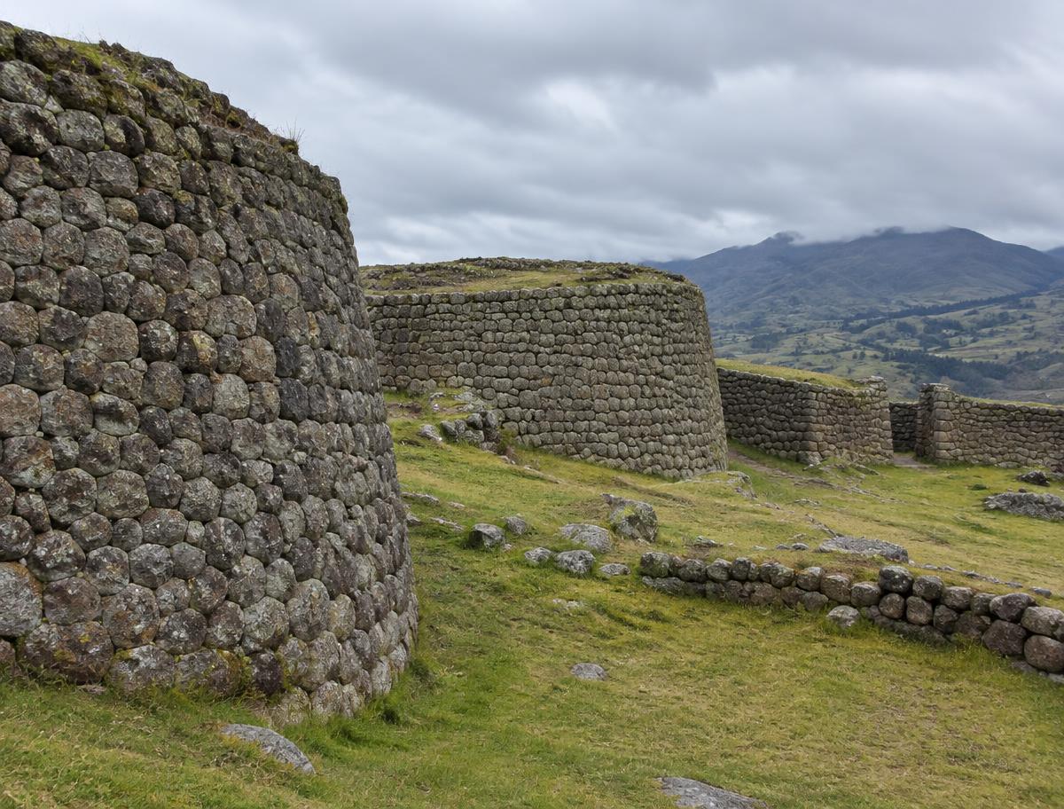 Tall curved fieldstone walls of Marcahuamachuco on a grassy plateau under cloud
